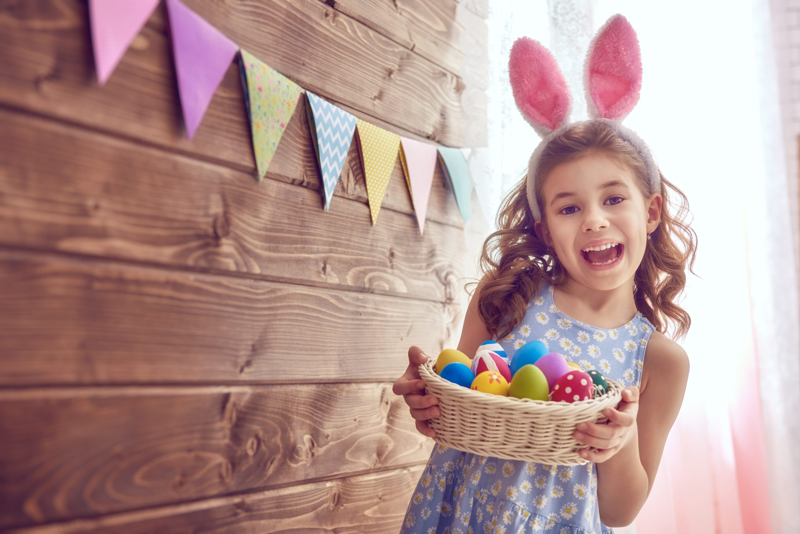 Cute little child wearing bunny ears on Easter day. Girl holding basket with painted eggs.