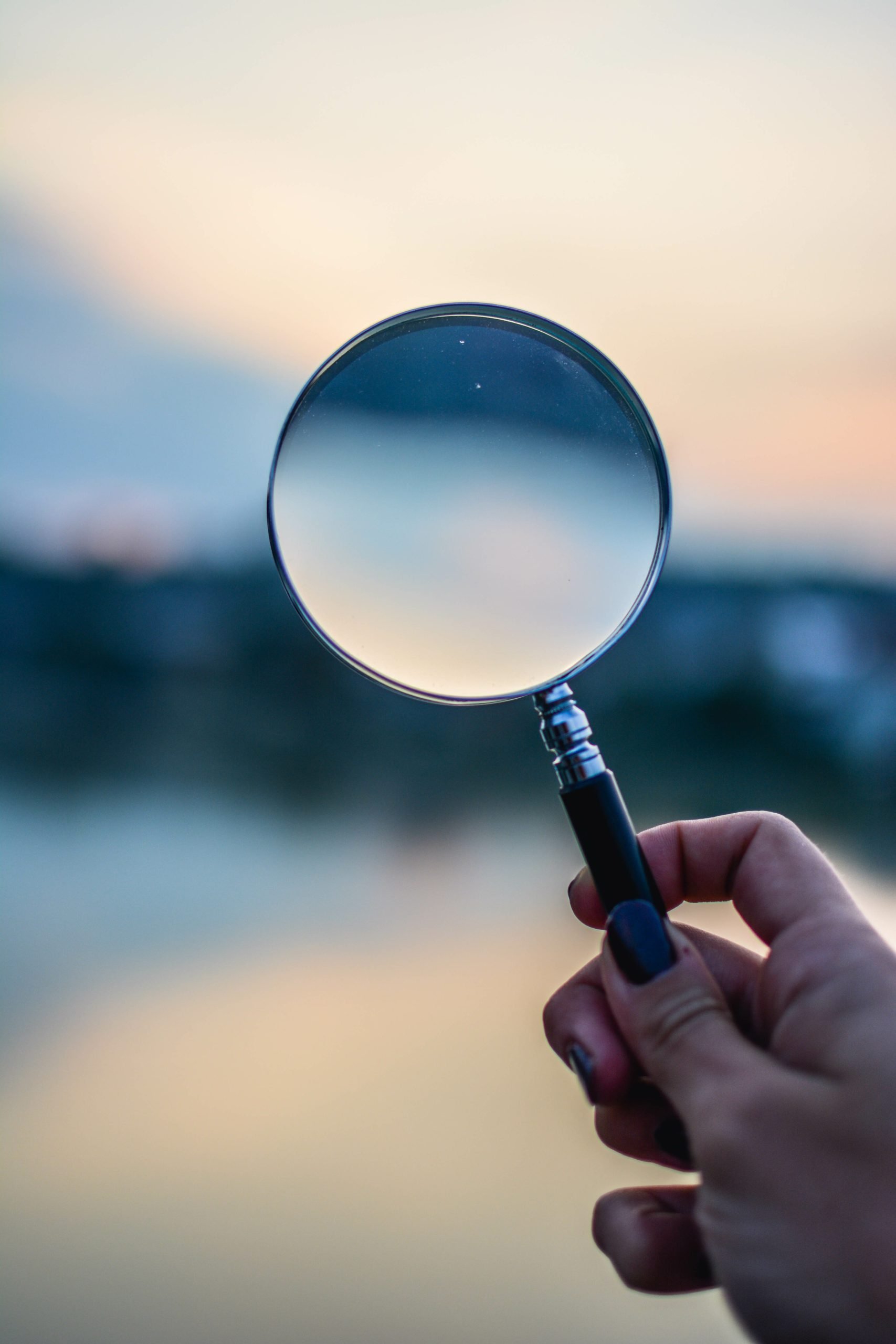 Close-Up Of Hand Holding Magnifying Glass Against Sky During Sun