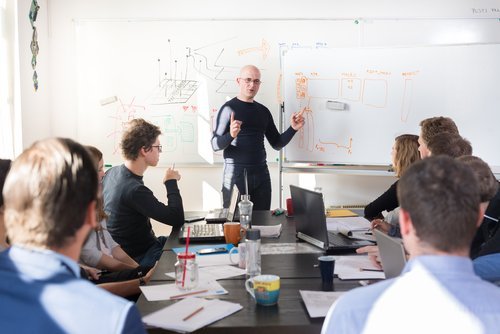 Boss running a productive team meeting to discuss B2B Digital Marketing for Tech Company with different strategies written on a white board.