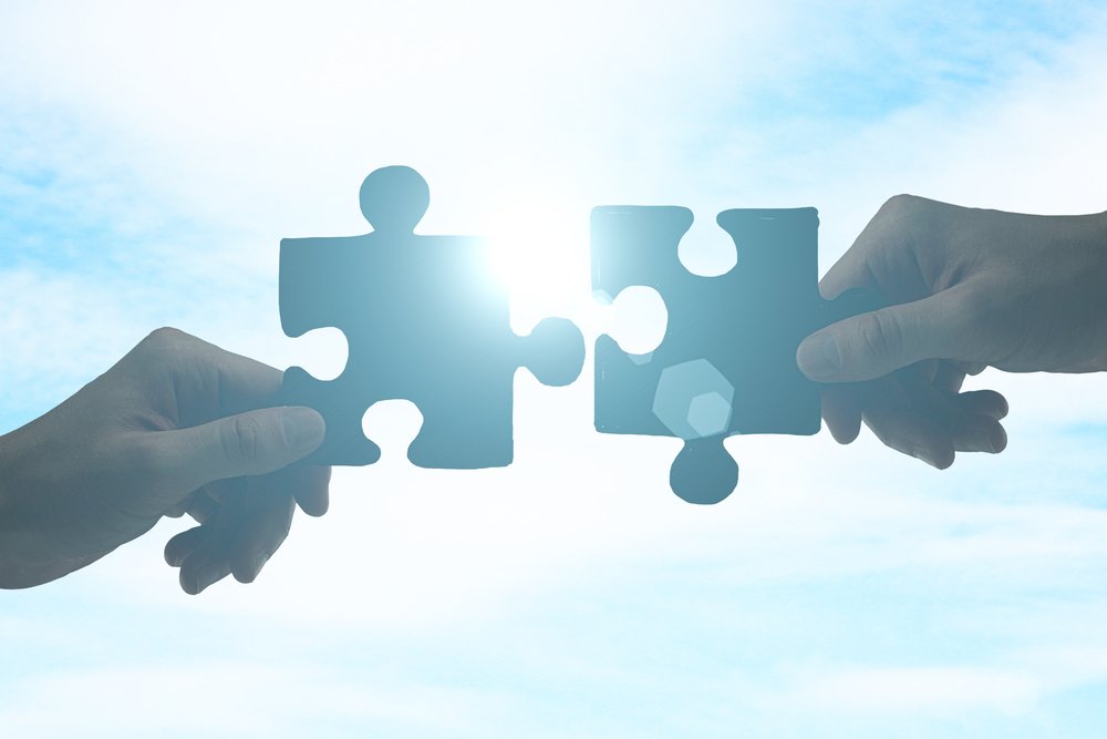 Partnership concept with hands putting puzzle pieces together on sky