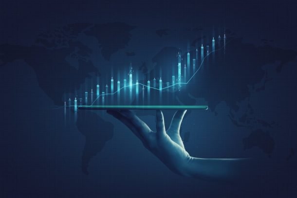 Hand holding a horizontal pad with a glowing bar graph rising up out of it in front of a map of the world.
