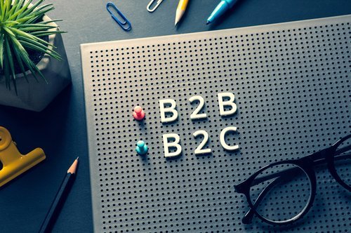 B2B and B2C letters, push pins and eyeglasses on a peg letter board on top of a desk with pens, paper clips and an indoor plant